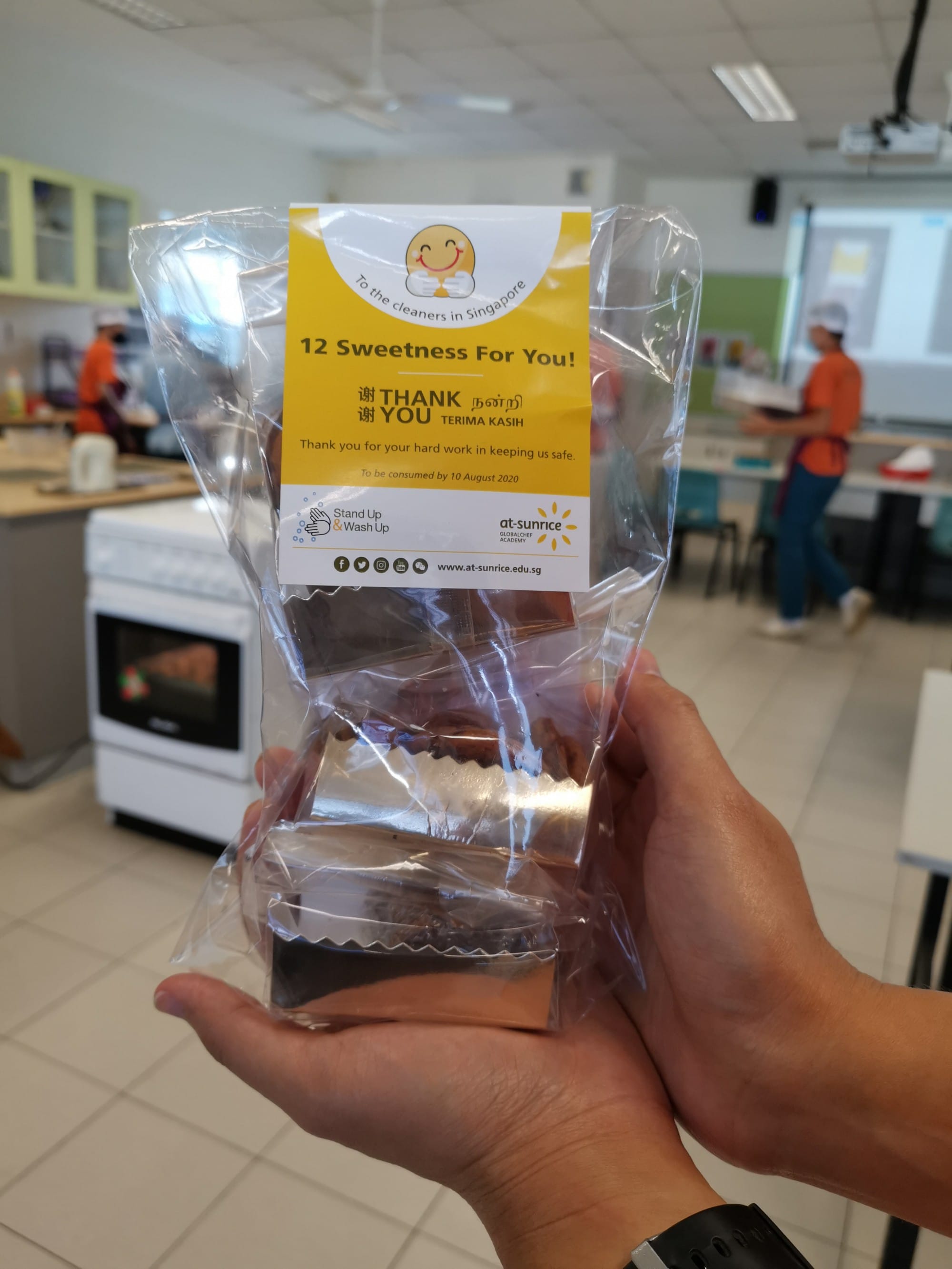 Hand holding a clear bag of chocolates labeled "12 Sweetness For You! Thank You" from at-sunrice academy.